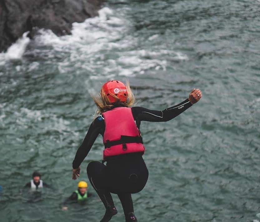 lady leaping into the sea in ilfracombe in wetsuit, helmet and buoyancy aid